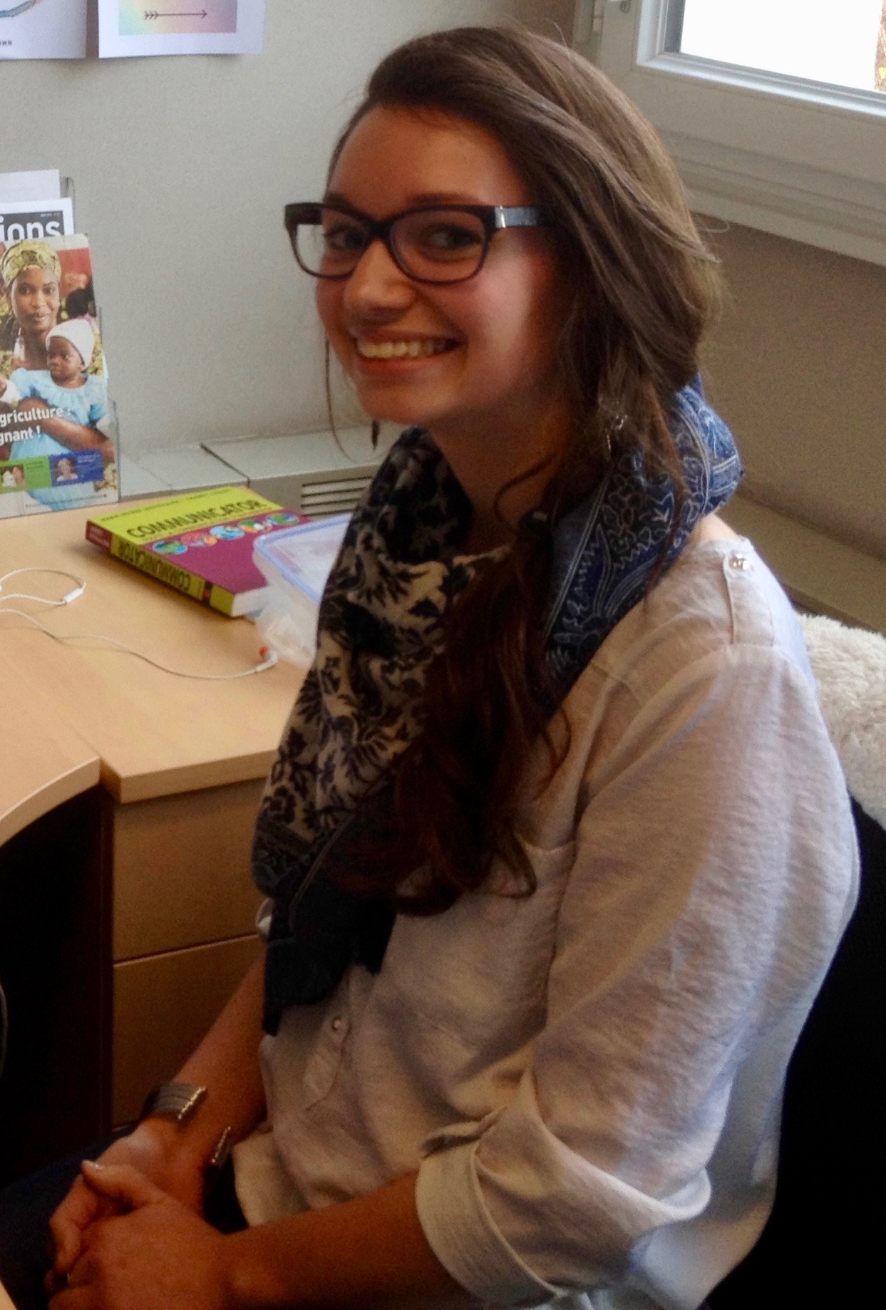 Elise is sitting down and smiling at the camera with her hair down to the side. She is wearing a white blouse and blue scarf.