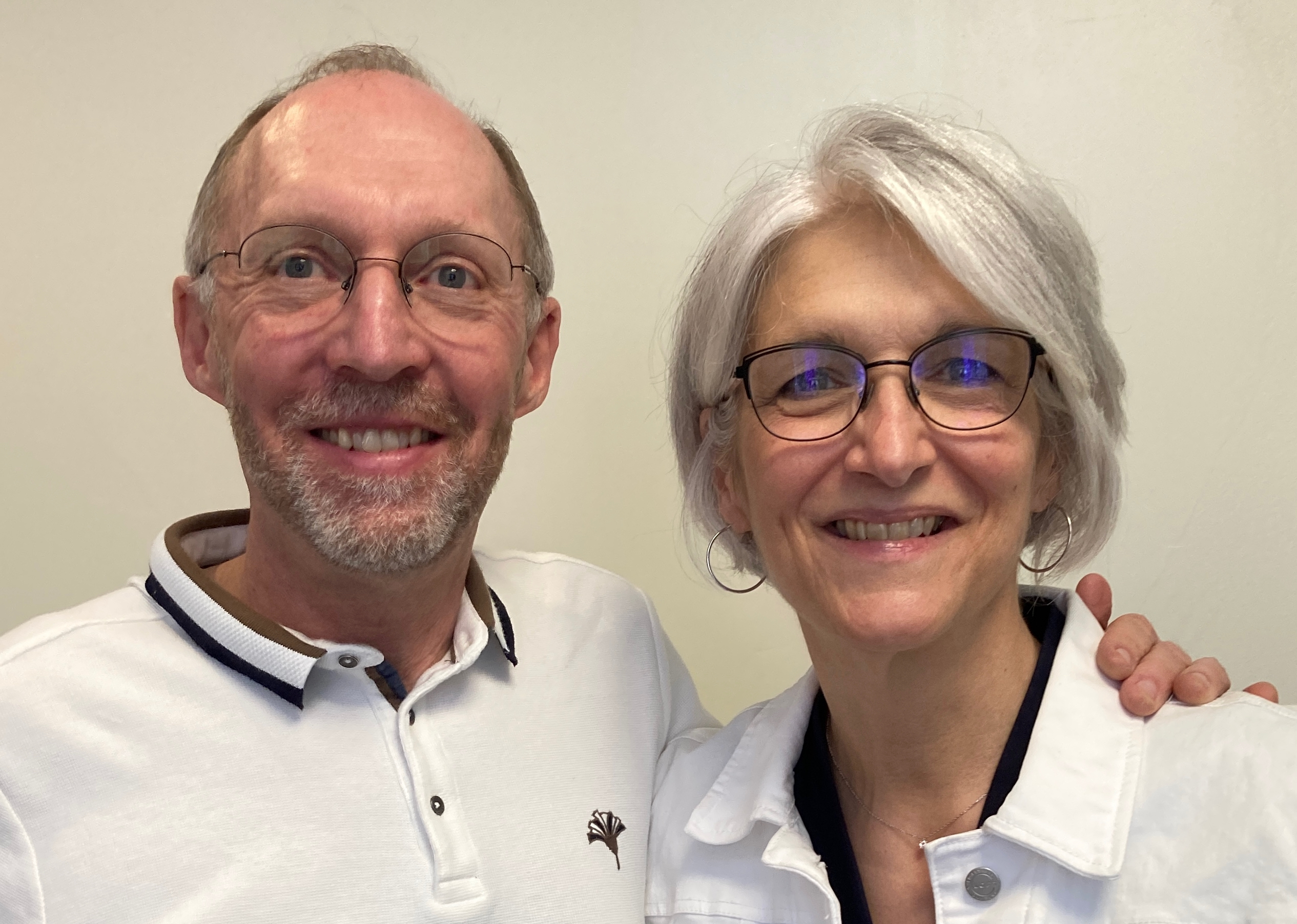 Close up of Paul with his arm around Louise in front of a tan wall.